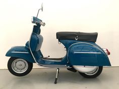 a blue scooter parked in a room with a white wall and black seat