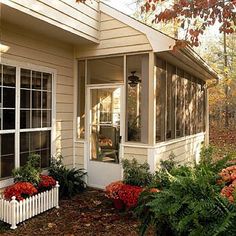 a small white house with red flowers in the front yard