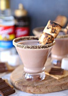 two glasses filled with chocolate and marshmallows on top of a wooden board