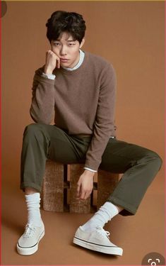 a young man sitting on top of a wooden block wearing white sneakers and a brown sweater