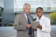 an older man and woman looking at something on a tablet computer outside a building with glass windows