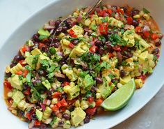 a white bowl filled with black beans, avocado and corn salad next to a lime wedge