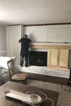 a man is working on a fireplace in a living room with white brick and wood