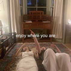 two women laying on the floor in front of a window with an inscription that reads, enjoy where you are