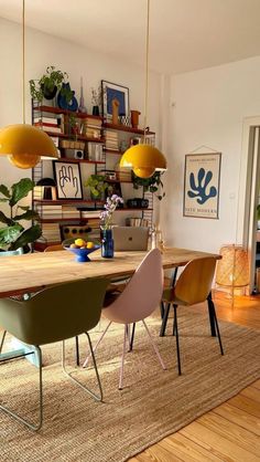 a dining room table with chairs and plants on the shelf above it, in front of a bookshelf