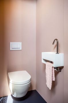 a white toilet sitting next to a sink in a pink walled bathroom with black flooring