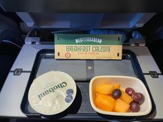 two bowls with fruit in them sitting on a tray next to a box of crackers