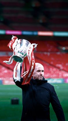 a man holding up a trophy on top of a field in front of an empty stadium