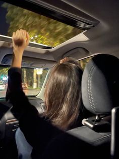 a woman driving a car at night with her hand up in the air and holding on to the dash board