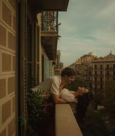 a man and woman standing on top of a balcony next to each other looking at each other