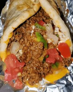 a burrito filled with meat and vegetables on top of tin foil