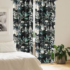 a white bed sitting next to a window covered in black and white floral print curtains