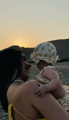 a woman holding a baby on the beach at sunset