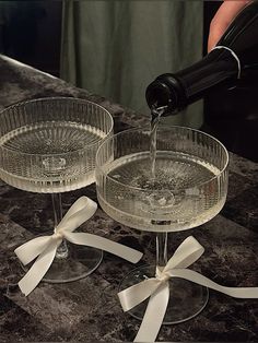 someone pouring wine into two glasses on top of a marble counter with white ribbons and bows