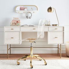 a white desk with gold accents and a clear chair in front of it on top of a rug