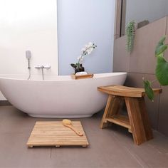 a white bath tub sitting next to a wooden stool and potted plant in a bathroom