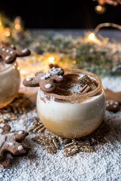 two cups filled with hot chocolate on top of snow covered ground next to christmas decorations