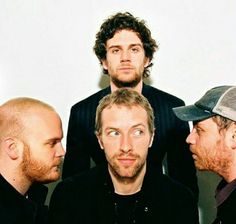 three men standing next to each other in front of a white wall with one looking at the camera