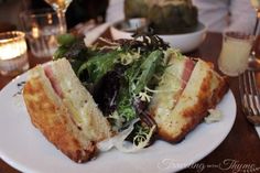 a sandwich cut in half sitting on top of a white plate next to a glass of wine