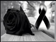 a black rose sitting on top of a wooden table next to a ribbon with an awareness symbol