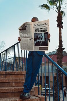 a man reading a newspaper while standing on some steps with palm trees in the background