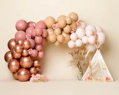 a teepee tent with balloons and flowers on the floor next to it, in front of a white wall