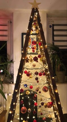 a decorated christmas tree with lights and ornaments on it's sides in front of a window