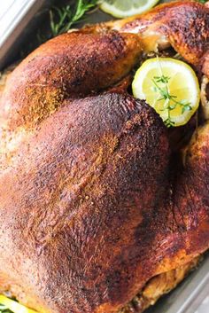 a roasted turkey in a roasting pan with lemons and herbs on the side