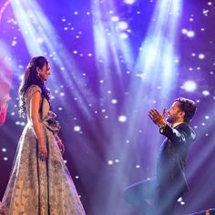 a man and woman performing on stage in front of bright lights with their hands together