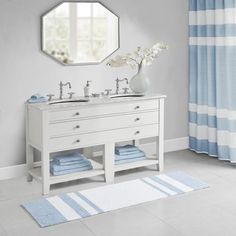 a white bathroom with blue and white towels on the floor, two sinks and a mirror