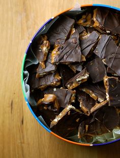 a bowl filled with chocolate pieces on top of a wooden table next to an orange and blue container