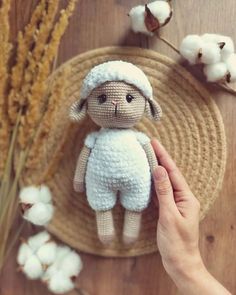 a hand holding a small stuffed animal on top of a wooden table next to cotton