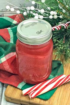 a glass jar filled with red liquid sitting on top of a wooden cutting board next to candy canes