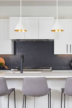 three gray chairs sitting in front of a kitchen island with white cabinets and black backsplash