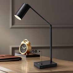 a desk lamp sitting on top of a wooden table next to a clock and wallet