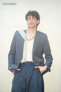 a man wearing a suit and tie standing in front of a wall with his hands on his hips