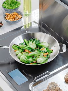 vegetables being cooked in a frying pan on a stove top with other food items