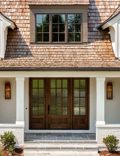 the front door of a house with two windows and brown shingles on it's roof