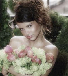 a woman with flowers in her hands is posing for a photo while holding some broccoli