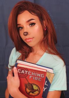 a woman holding a book with her nose painted like a cat's eye and the words catching fire written on it