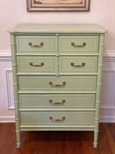 a green dresser sitting on top of a hard wood floor next to a framed painting