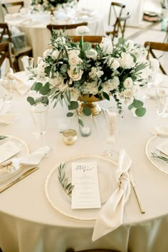 the table is set with white flowers and greenery for an elegant centerpieces