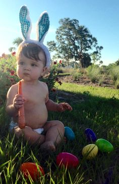 a baby sitting in the grass with an easter bunny hat on and holding a carrot