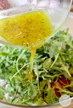 a salad with dressing being poured into it and on top of the salad in a glass bowl