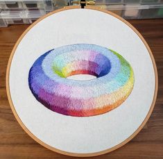 an embroidery project with a circular design on the front and back of it, sitting on top of a wooden table