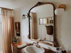 a bathroom sink sitting under a large mirror next to a bath room window with curtains