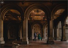 an engaged couple standing in the middle of a large building with columns and arches on either side