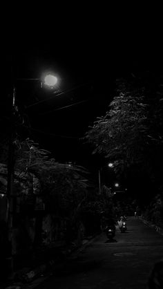 black and white photograph of street at night with cars parked on the side of the road