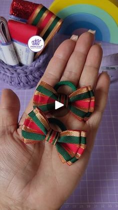 a hand holding a small red, green and gold bow