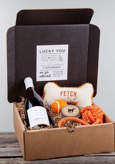 a wine bottle and some food in a box on a wooden table next to a pillow